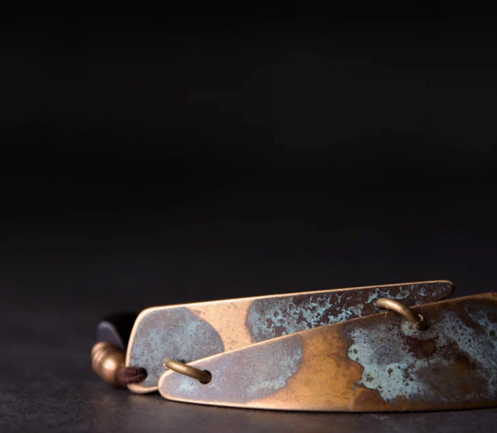 Close-up of vintage brass plate with copper patina on ebony wood bead bracelet, showcasing handcrafted texture detail