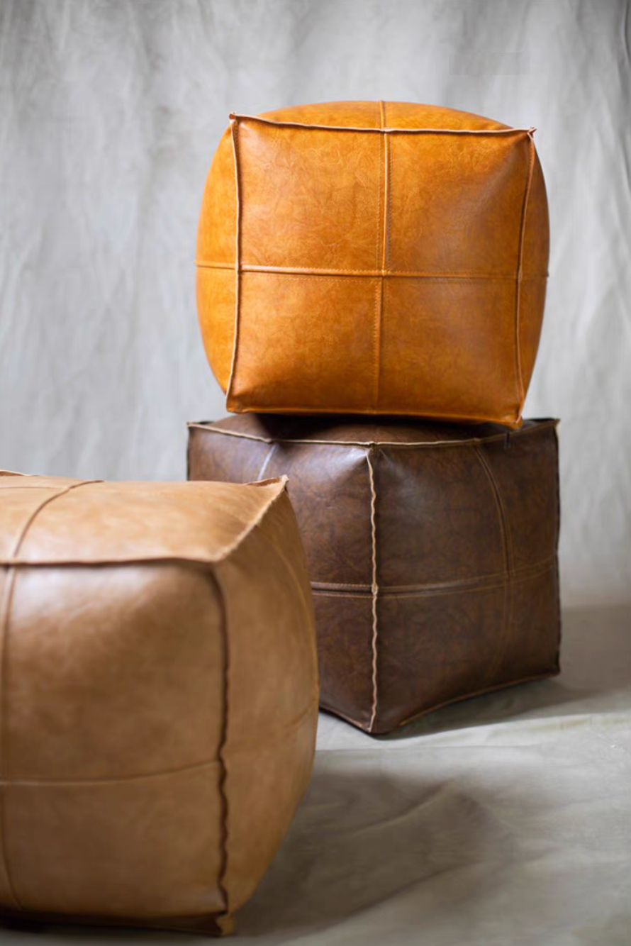 Multicolor faux leather square poufs in orange yellow, dark brown, and khaki stacked together in a styled display