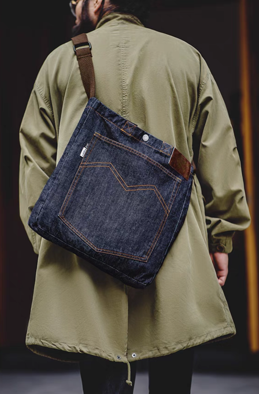 Person wearing denim messenger tote bag crossbody showing back view with large pocket and adjustable strap
