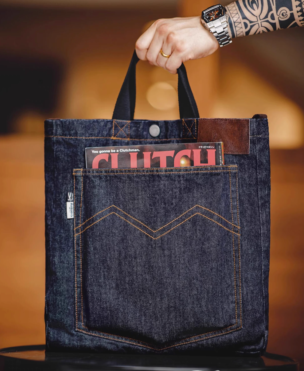 Vintage-inspired denim messenger tote bag in denim blue with front pocket holding magazine and top handle view