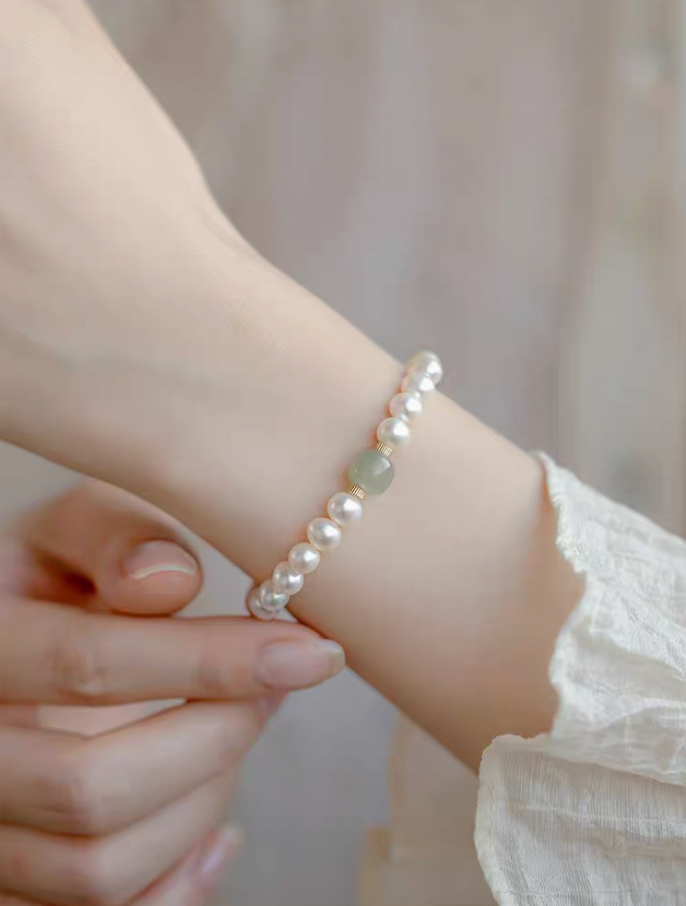 Close-up of hand adjusting jade and pearl bracelet on wrist, showing fit and refined craftsmanship.