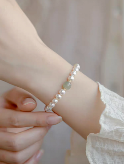 Close-up of hand adjusting jade and pearl bracelet on wrist, showing fit and refined craftsmanship.