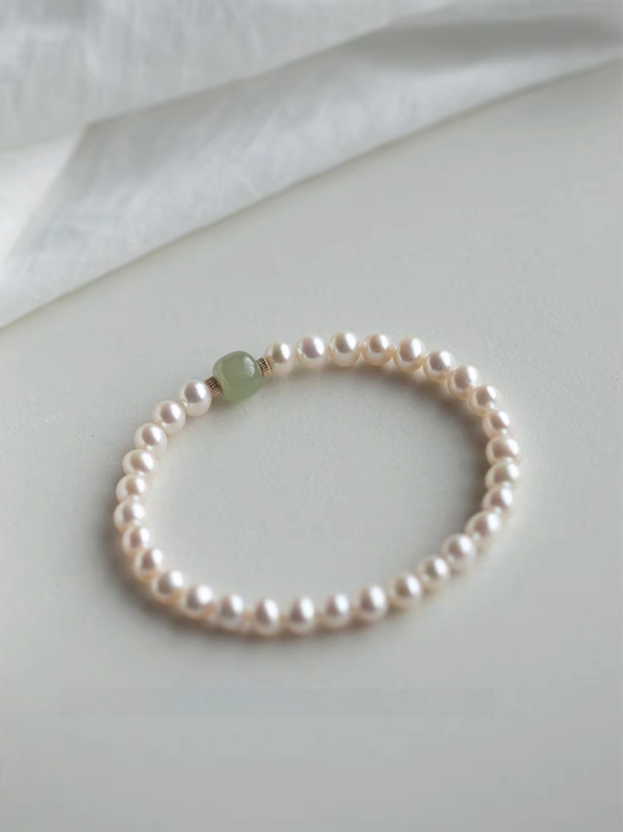 Flat lay of jade and pearl bracelet in natural color on soft neutral fabric background, highlighting minimal design.