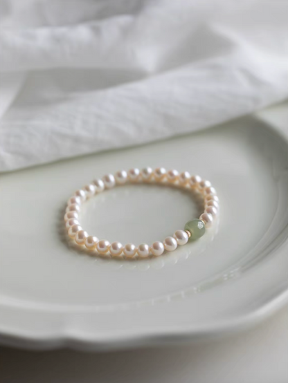 Bracelet displayed on ceramic plate showing natural color pearls with central jade bead in soft lighting.