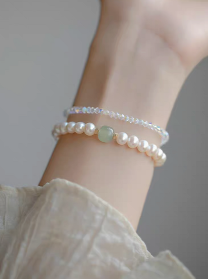 Wrist shot of jade and pearl bracelet styled with another bracelet, showcasing layered jewelry look.