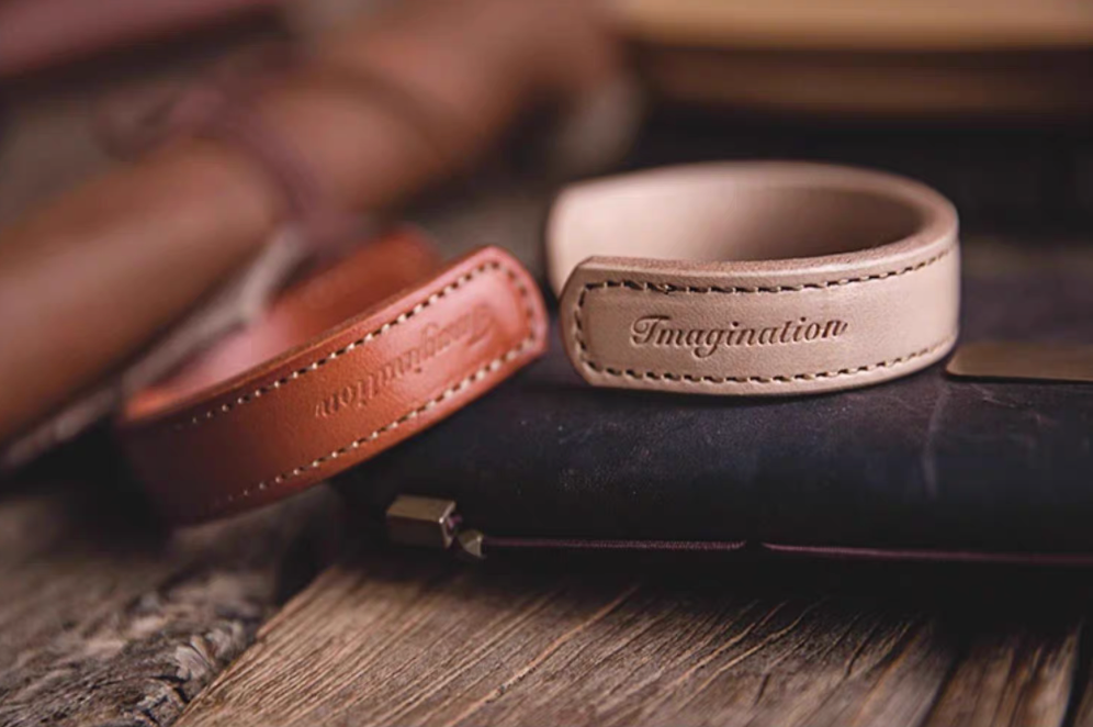 Dark brown and pink leather cuff bracelets placed on leather wallet lifestyle scene showing embossed imagination detail