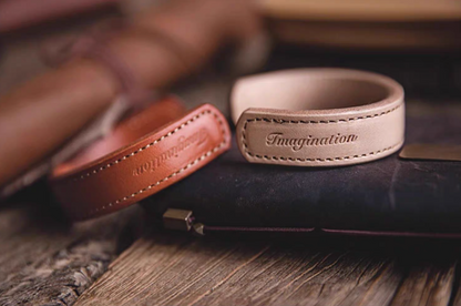 Dark brown and pink leather cuff bracelets placed on leather wallet lifestyle scene showing embossed imagination detail