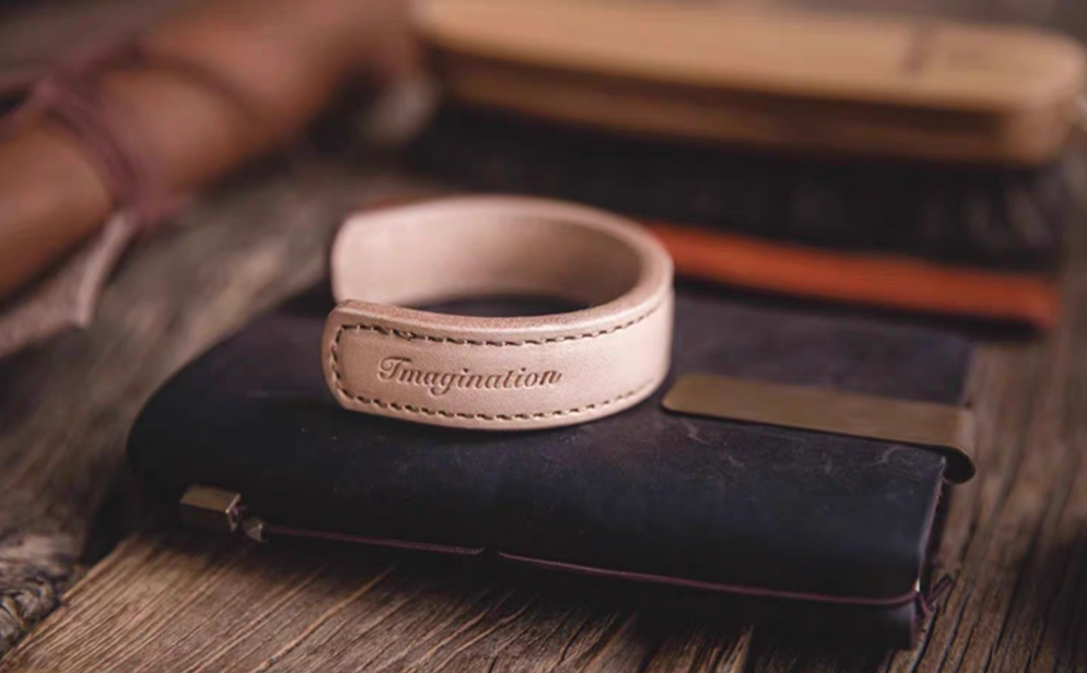 Pink leather cuff bracelet placed on leather wallet lifestyle view showing imagination engraving