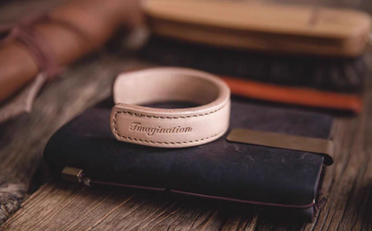 Pink leather cuff bracelet placed on leather wallet lifestyle view showing imagination engraving