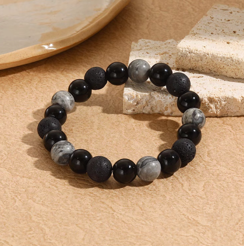 Black lava stone bracelet with porous lava beads, smooth black beads, and gray natural stone accents styled on textured surface
