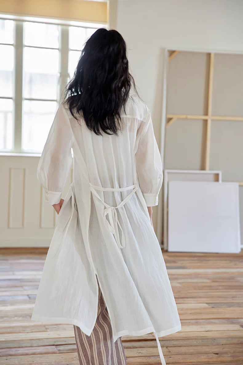 Back view of White pleated midi dress styled open with layered outfit, highlighting soft drape, pleated structure, and airy movement