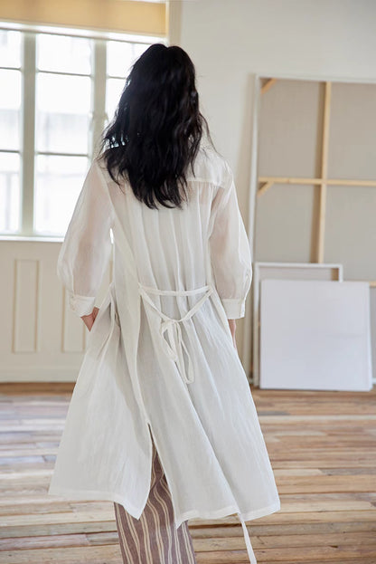 Back view of White pleated midi dress styled open with layered outfit, highlighting soft drape, pleated structure, and airy movement