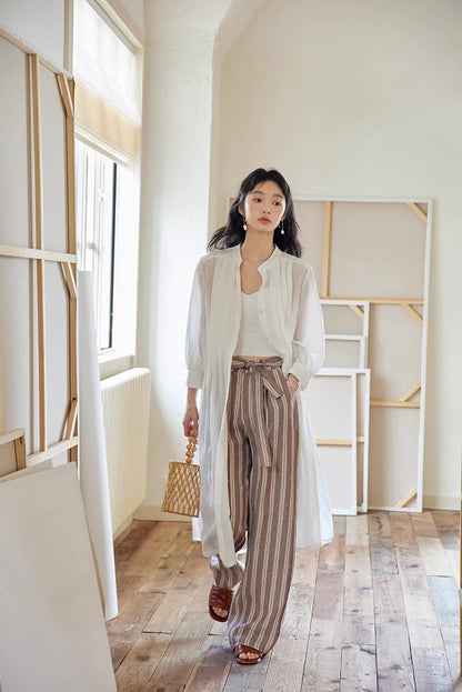 White pleated midi dress worn open as layering piece over striped pants, showcasing versatile styling and lightweight breathable fabric