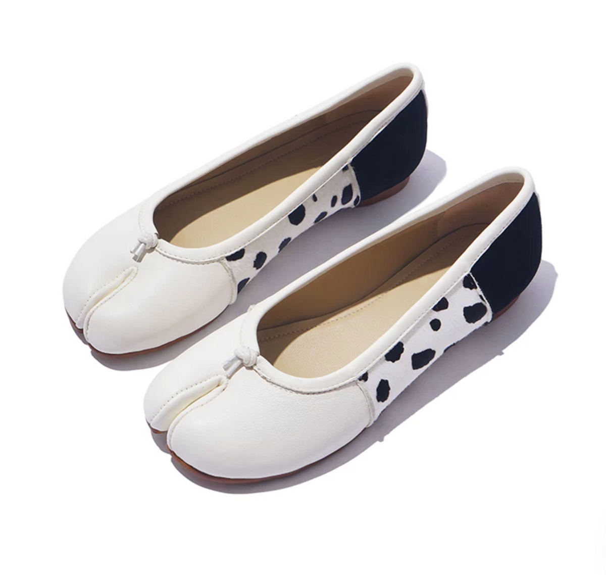 Pair of White split-toe ballet flats with black-spotted horsehair side panels and black suede heels, angled view