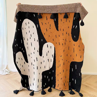 Wild cactus luxe throw blanket fully displayed with abstract cactus shapes in black, white, and warm orange tones with tassel edges