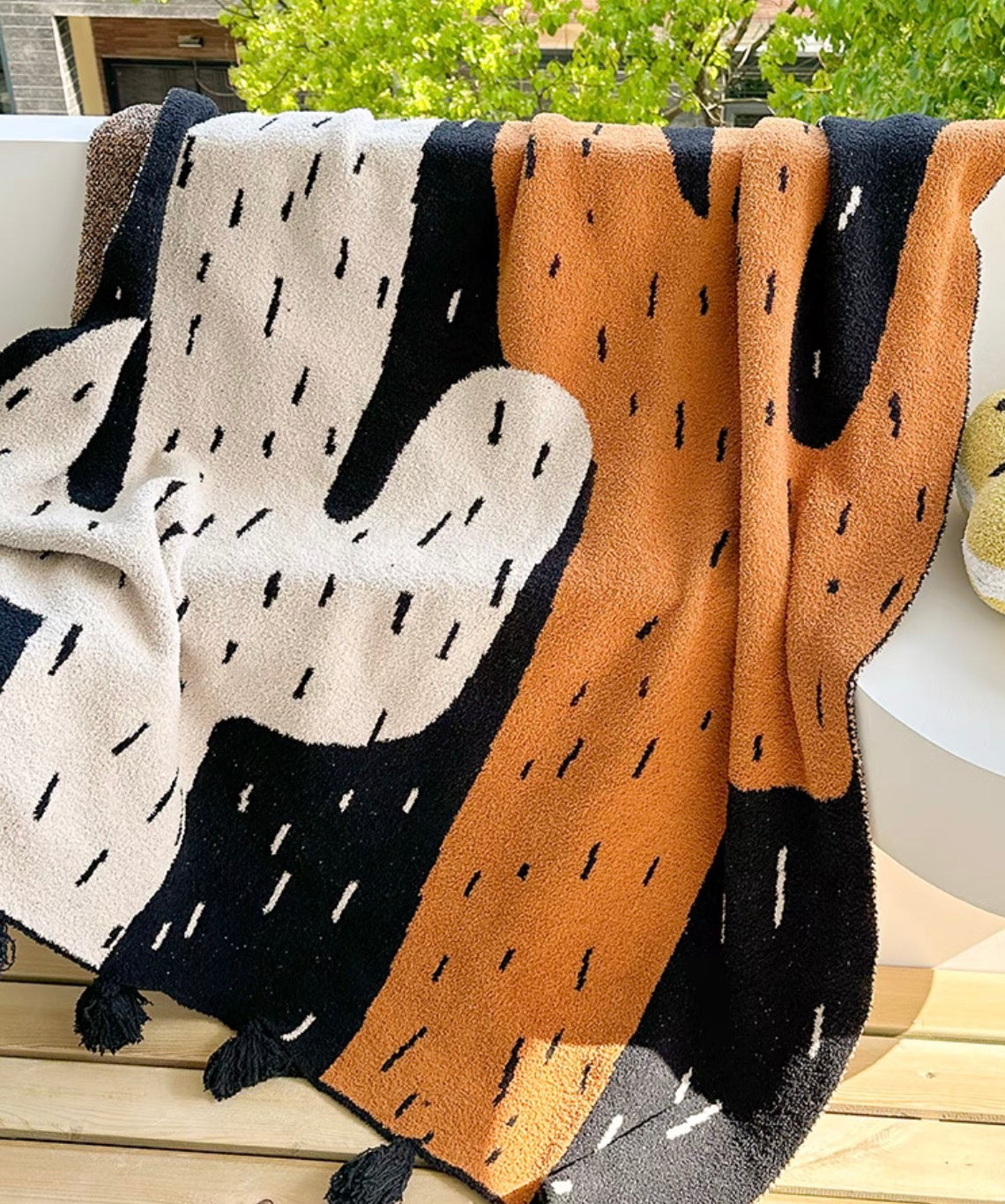 Wild cactus throw blanket draped over outdoor bench in sunlight, showcasing large cactus pattern and soft plush material