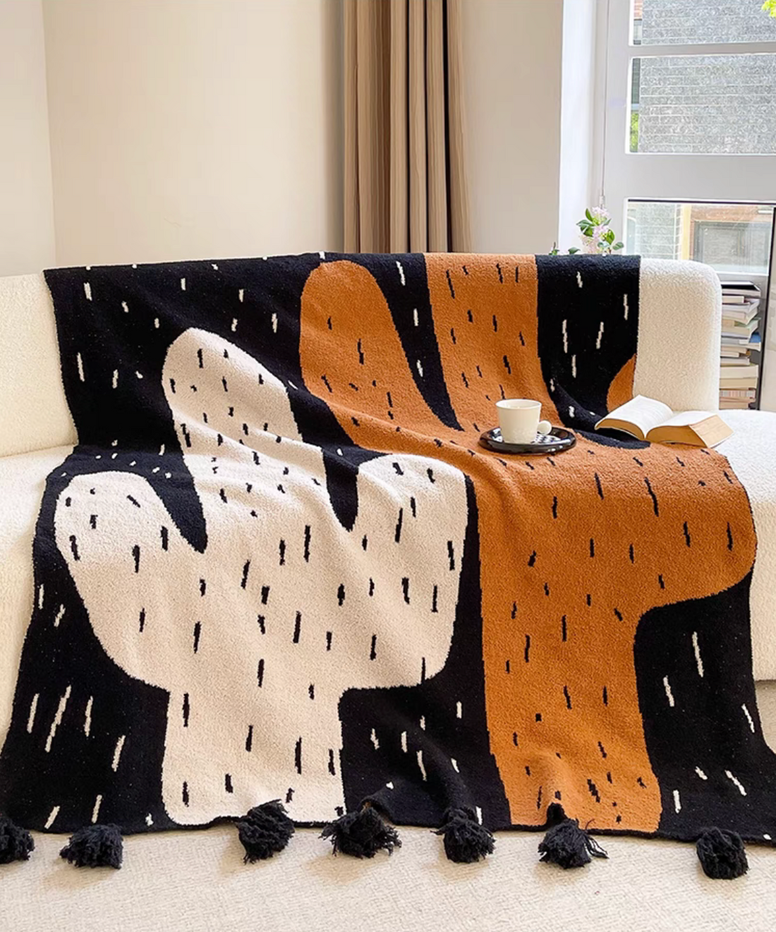 Wild cactus throw blanket draped over sofa with coffee cup and book, showing cozy plush texture and bold cactus-inspired pattern