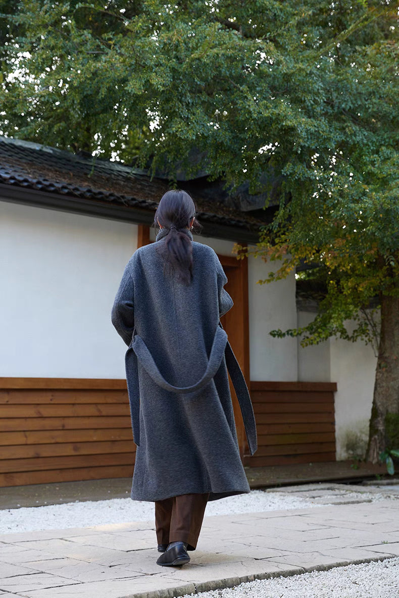 Back view of dark gray long Willow Lane Wool Coat outdoors, showcasing belt detail, clean tailoring, and mid-calf length design