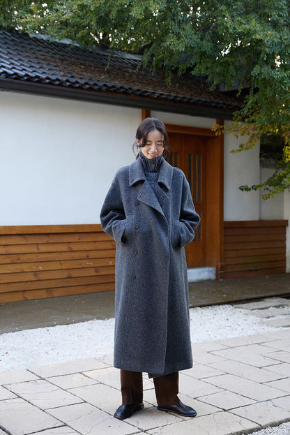 Woman wearing Willow Lane Wool Coat in dark gray long style standing outdoors, featuring wrap design, soft wool fabric, and minimalist elegance
