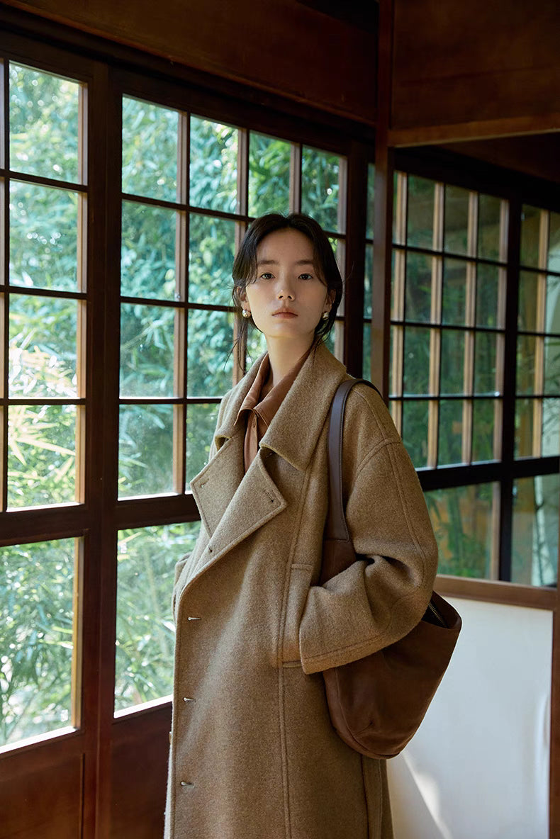 Woman wearing khaki long Willow Lane Wool Coat in side view with shoulder bag, highlighting slanted lapel, structured silhouette, and refined wool fabric