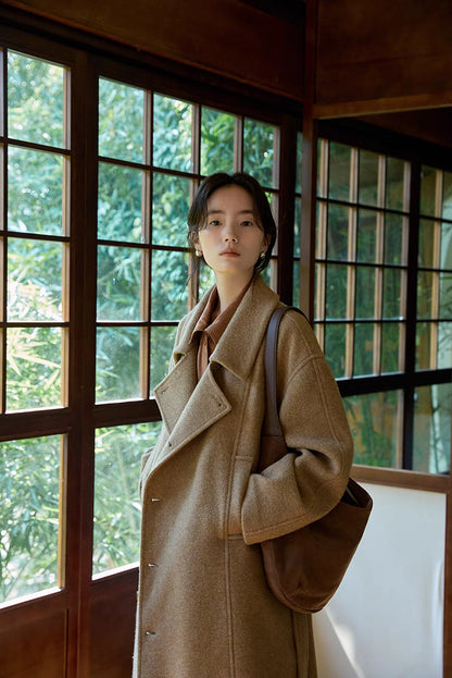 Woman wearing khaki long Willow Lane Wool Coat in side view with shoulder bag, highlighting slanted lapel, structured silhouette, and refined wool fabric