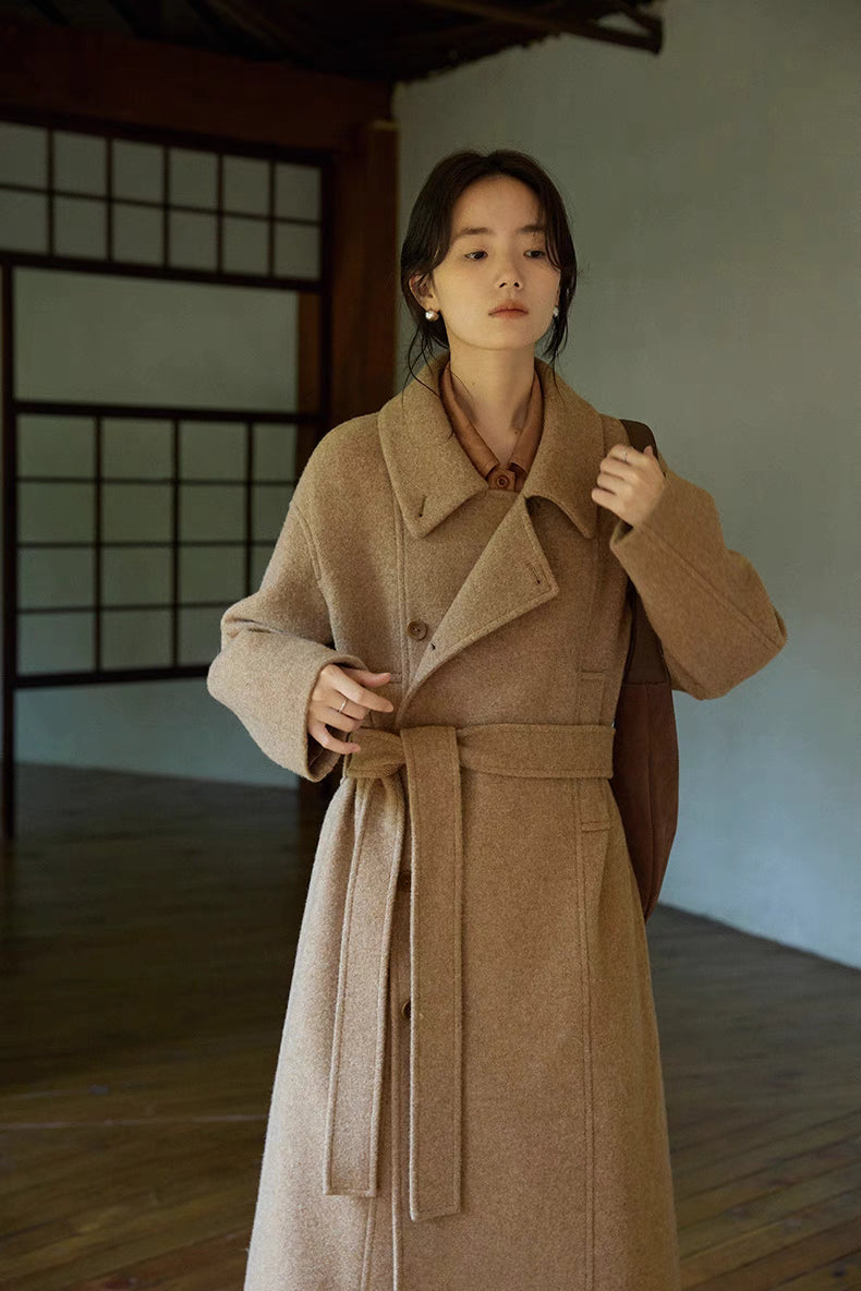 Woman wearing Willow Lane Wool Coat in khaki long style standing indoors, featuring wrap design, belted waist, and soft wool texture for elegant everyday wear