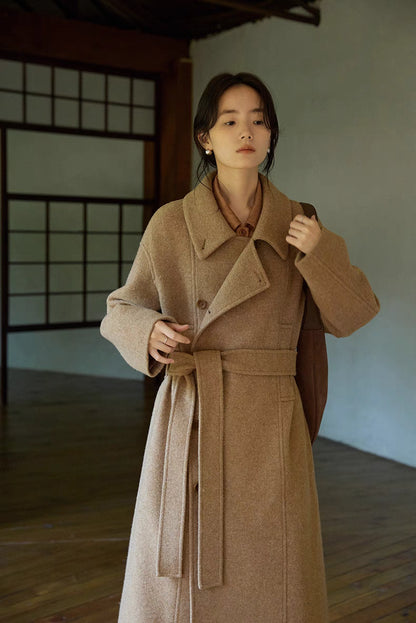 Woman wearing Willow Lane Wool Coat in khaki long style standing indoors, featuring wrap design, belted waist, and soft wool texture for elegant everyday wear