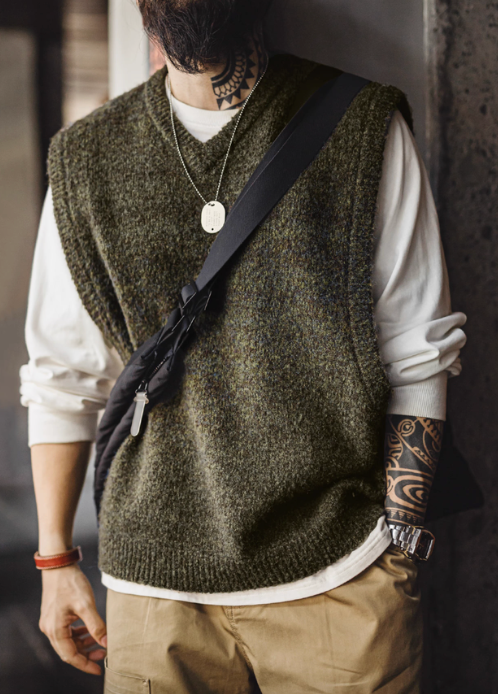 Model wearing Woodland Retro V-Neck Vest in Moss Green layered over white long sleeve shirt with crossbody bag front view