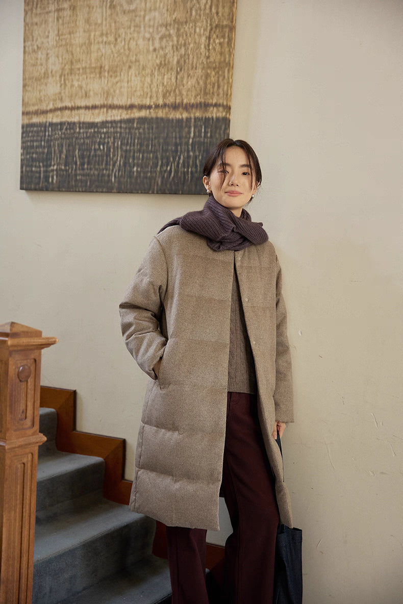 woman wearing wool-blend long down coat standing by staircase indoors