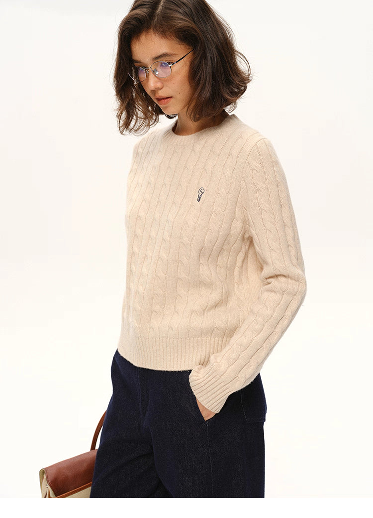 Model wearing beige almond wool cable-knit sweater with navy pants