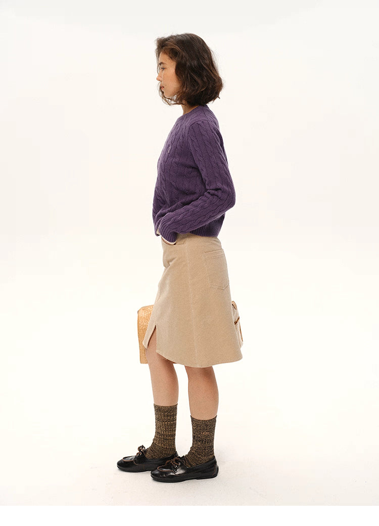 Side profile of model wearing deep purple wool cable sweater and beige skirt