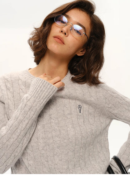 Close-up of light gray wool sweater showing cable texture and embroidered logo