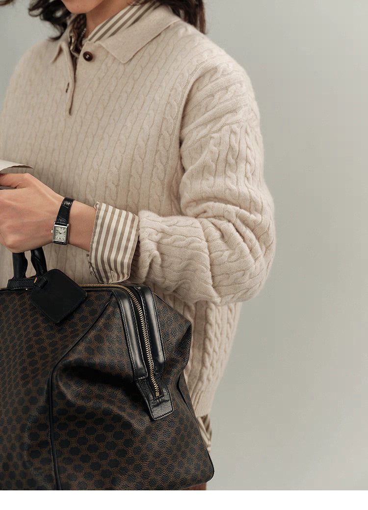 Beige cable-knit wool polo sweater layered over striped shirt cuffs, holding patterned leather bag