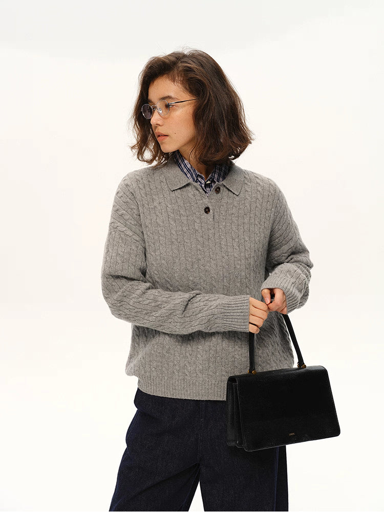 Model in grey wool cable-knit polo sweater holding a black structured handbag