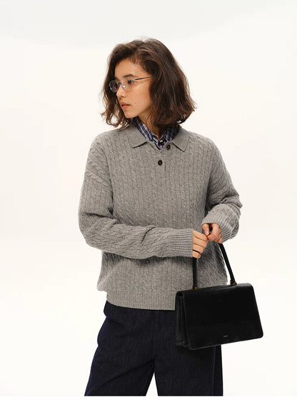 Model in grey wool cable-knit polo sweater holding a black structured handbag