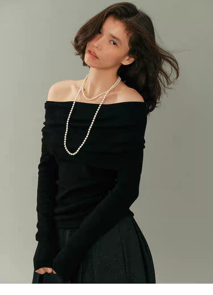 Model wearing black off-shoulder wool top with long pearl necklace on grey background