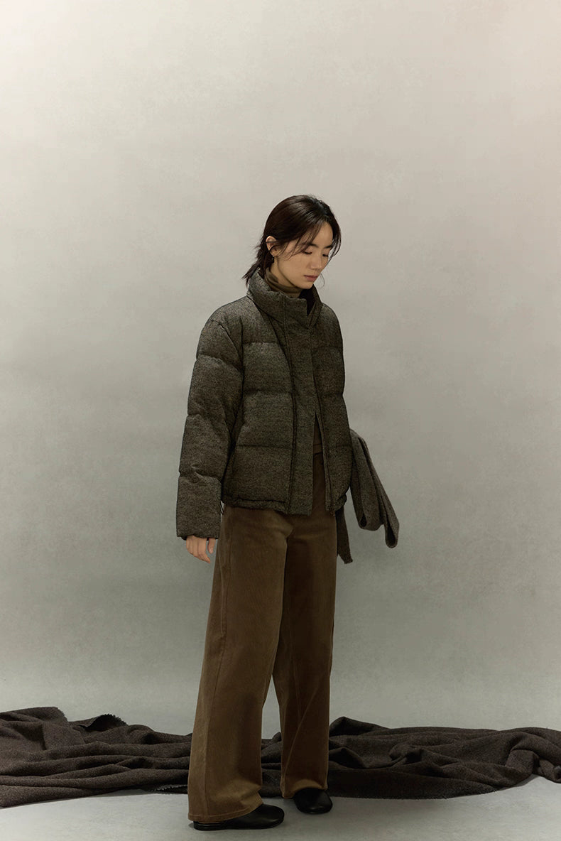 Woman standing in wool-blend down jacket holding matching wool scarf.