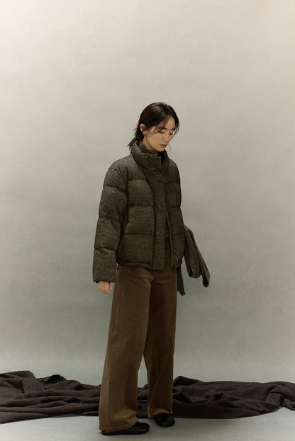 Woman standing in wool-blend down jacket holding matching wool scarf.
