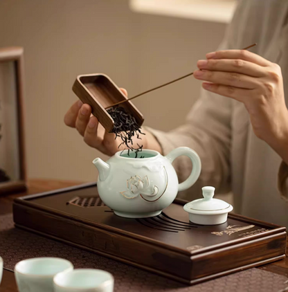 Yingqing Lotus Relief Ceramic Teapot in white with lid removed as loose tea leaves are added using a wooden scoop on a tea tray setup