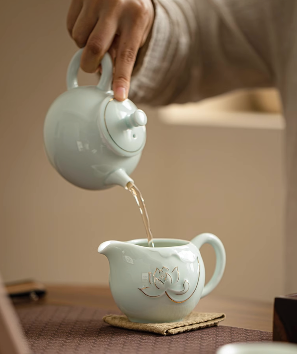 Yingqing Lotus Relief Ceramic Teapot in white pouring tea into a matching ceramic pitcher with lotus relief design on a wooden tea table