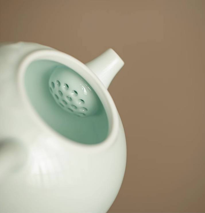 Close-up of Yingqing Lotus Relief Ceramic Teapot in white showing built-in spout filter holes and smooth glazed interior detail